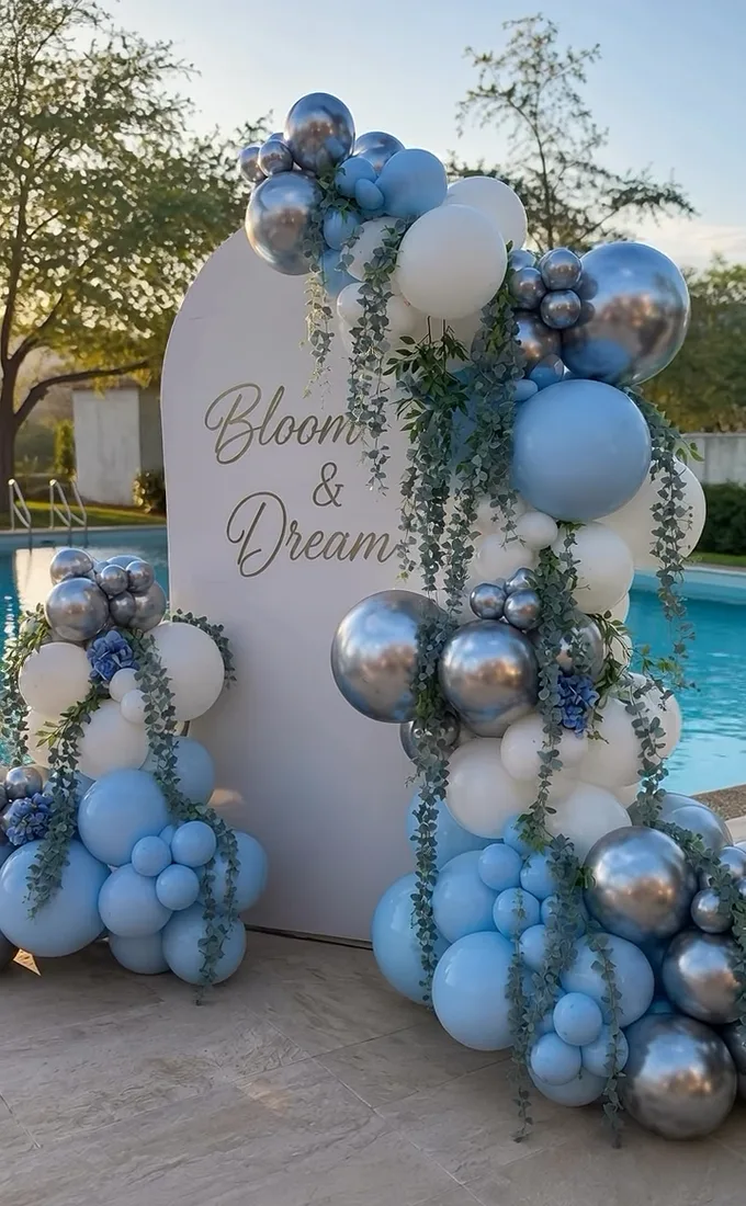 Guirnalda de globos azules, blancos y plateados cayendo por el costado de un backdrop.