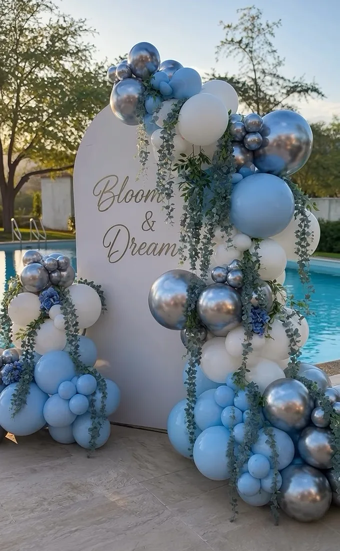 Backdrop blanco con globos azules y plateados frente a una alberca, a contraluz.