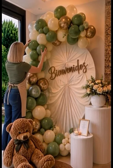 Montaje de bienvenida con letrero, globos verde salvia y dorados y arreglos florales.