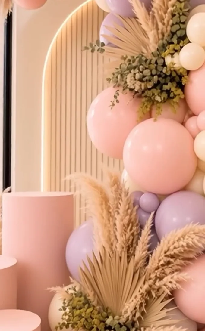 Pedestales en rosa palo frente a un arco acanalado con globos, pampas y follaje seco.