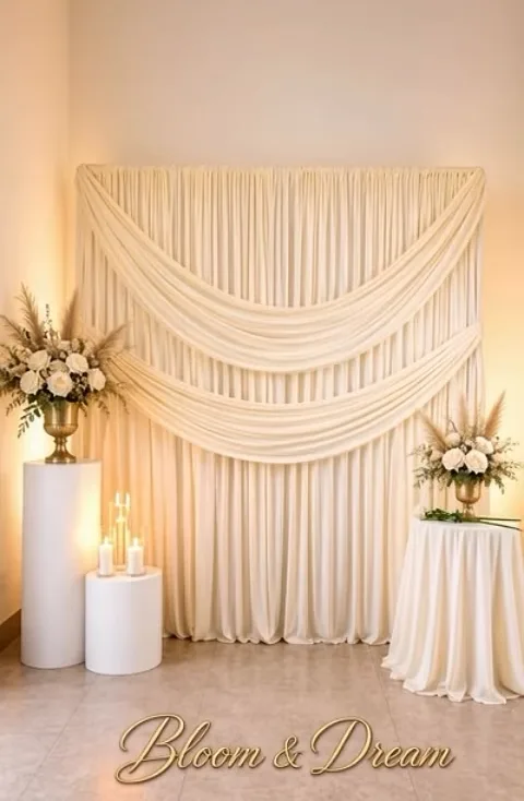 Backdrop de telas en marfil con caída amplia, velas encendidas y arreglos florales sobre pedestales.