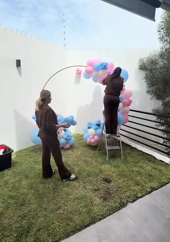 Dos personas del equipo montando un aro de globos en rosa y azul en un jardín.