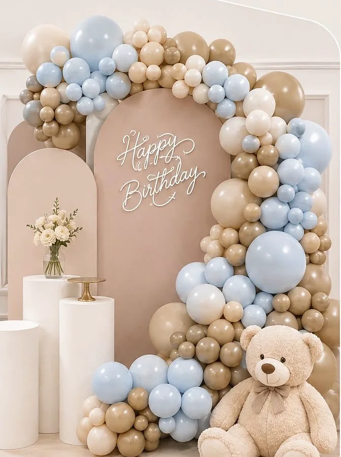 Backdrop en beige con letrero «Happy Birthday», guirnalda orgánica de globos en azul, latte y beige, cilindros blancos y flores.