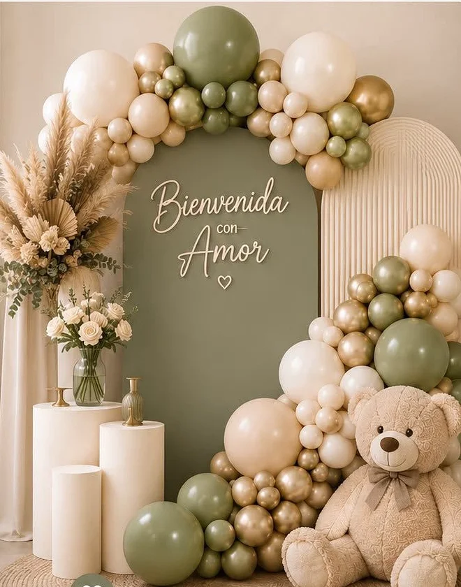 Backdrop en verde salvia con letrero «Bienvenida con Amor», guirnalda orgánica de globos en salvia, crema y dorado, cilindros y pampas.