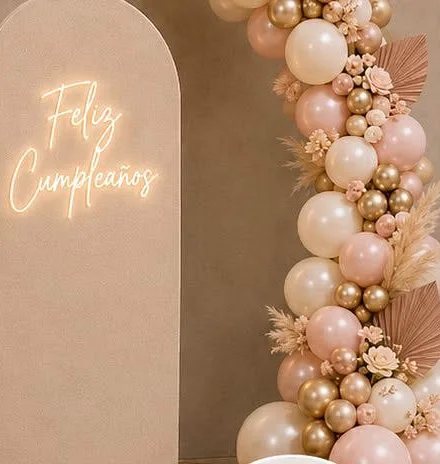 Mampara forrada en tela beige con letrero LED «Feliz Cumpleaños» y guirnalda orgánica de globos en rosa, ivory y dorado con pampas.