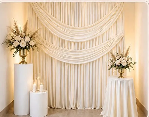 Escenario drapeado en tonos marfil con arreglos florales sobre pedestales, mesa forrada y velas LED.